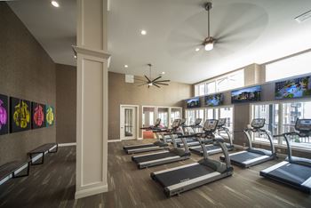 A gym with treadmills and televisions on the wall